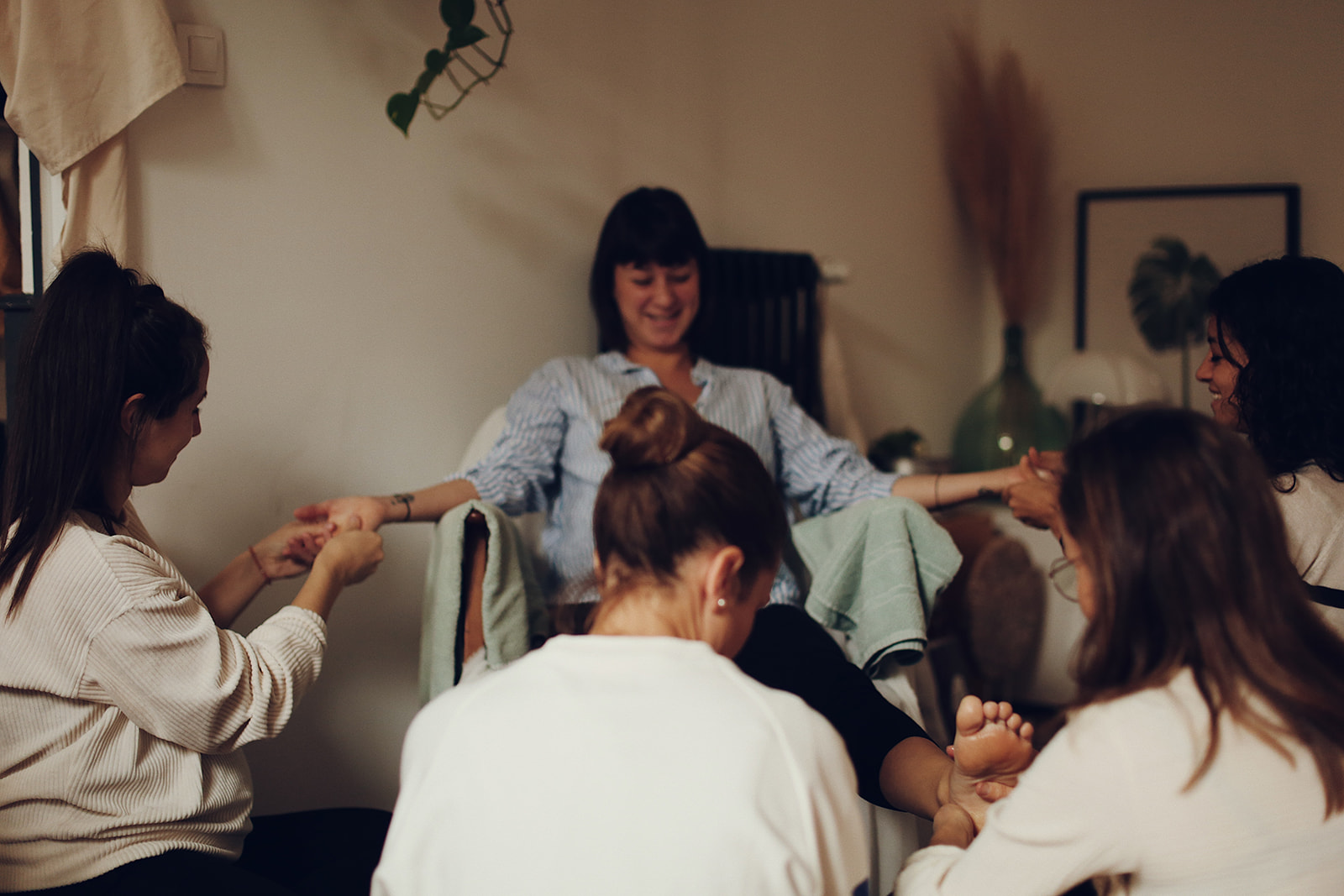 photo d'un célébration de fin de grossesse. une femme enceinte avec le sourire assise sur un fauteuil, en train de se faire masser par plusieurs autres femmes. on en voit 4 sur la photo, elles massent ses mains et ses pieds. Massage à 8 mains. Doula Arles Tarascon