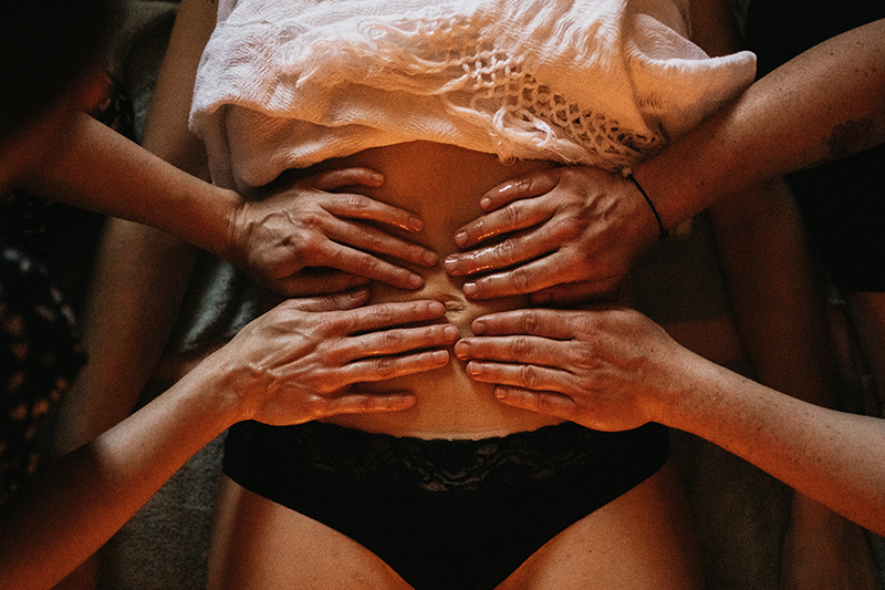 massage à quatre mains. photo d'un soin rituel de fermeture, type rebozo. Deux femmes entrain de masser le ventre d'une autre femme allongée sur le dos. Doula Arles Tarascon